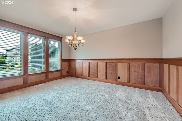 unfurnished room featuring a notable chandelier, light carpet, and wooden walls