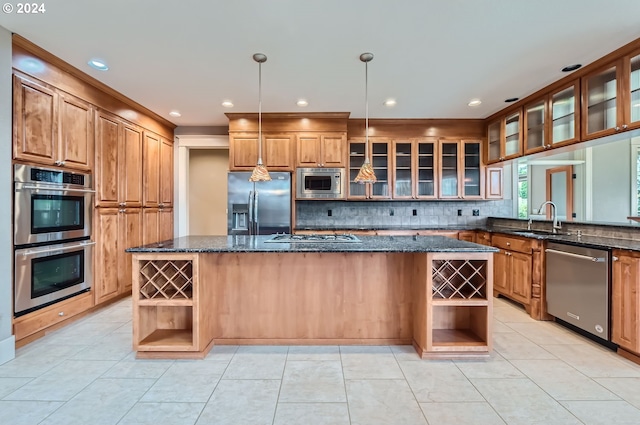 kitchen featuring stainless steel appliances, light tile patterned flooring, dark stone countertops, hanging light fixtures, and an island with sink