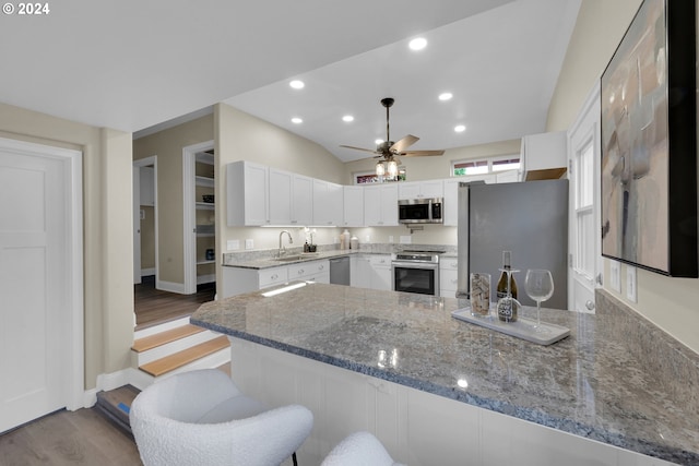 kitchen with appliances with stainless steel finishes, kitchen peninsula, vaulted ceiling, white cabinets, and light stone counters