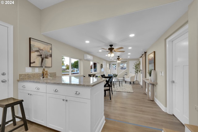 kitchen featuring kitchen peninsula, ceiling fan, white cabinets, light stone counters, and light hardwood / wood-style flooring