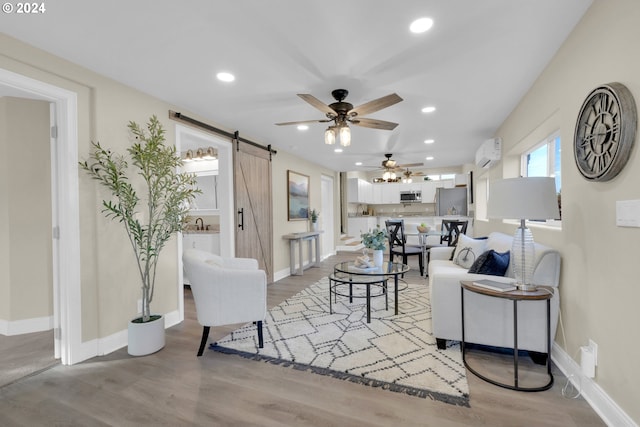 living room with a wall unit AC, a barn door, light wood-type flooring, and ceiling fan