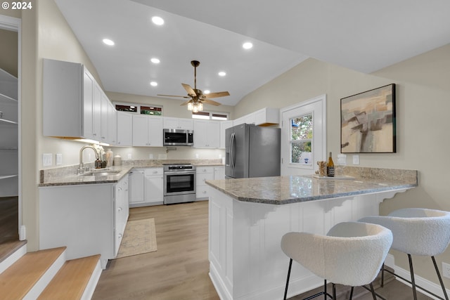 kitchen with white cabinets, appliances with stainless steel finishes, a kitchen breakfast bar, light hardwood / wood-style floors, and sink