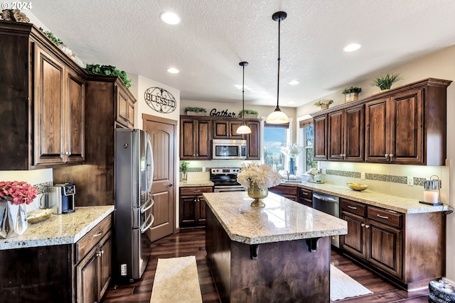 kitchen featuring stainless steel appliances, dark brown cabinets, hanging light fixtures, a kitchen island, and dark hardwood / wood-style flooring