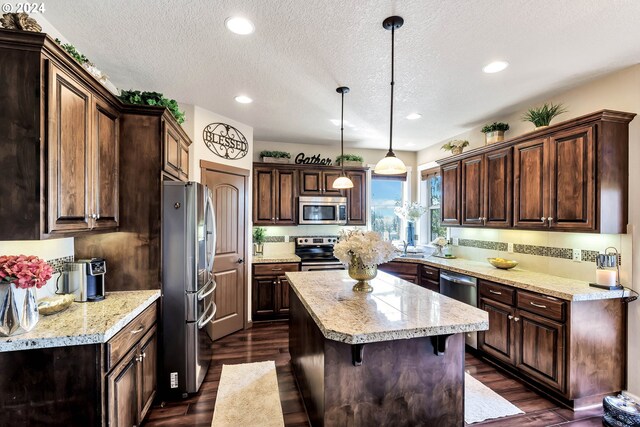 kitchen with dark wood-type flooring, dark brown cabinetry, decorative light fixtures, appliances with stainless steel finishes, and a kitchen island