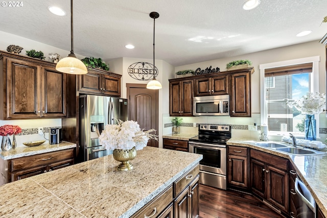 kitchen with sink, appliances with stainless steel finishes, decorative light fixtures, and dark hardwood / wood-style floors