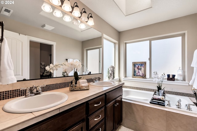 bathroom with a relaxing tiled tub and dual bowl vanity