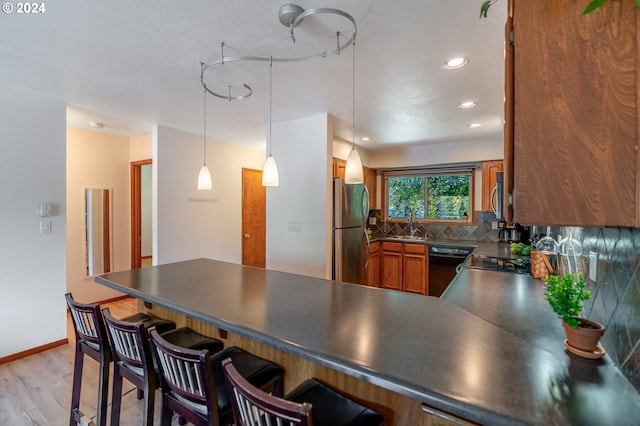 kitchen featuring sink, decorative backsplash, appliances with stainless steel finishes, light hardwood / wood-style floors, and kitchen peninsula