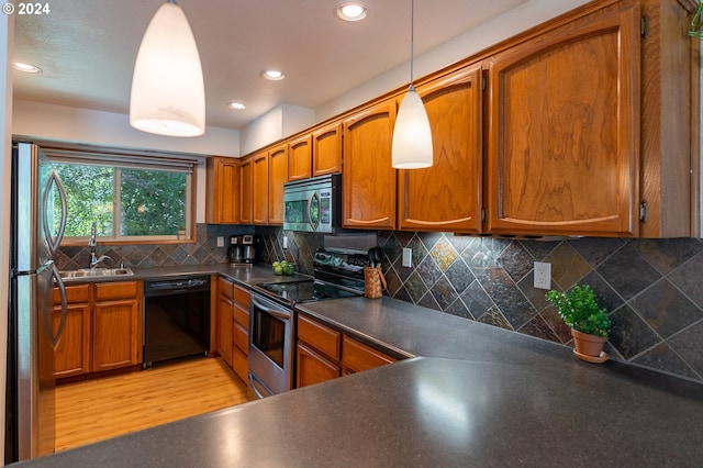 kitchen featuring backsplash, sink, hanging light fixtures, light wood-type flooring, and stainless steel appliances