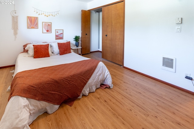 bedroom with heating unit, hardwood / wood-style flooring, and a closet