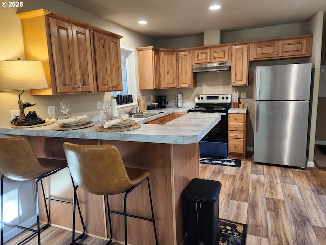 kitchen featuring a kitchen bar, sink, light hardwood / wood-style flooring, kitchen peninsula, and stainless steel appliances