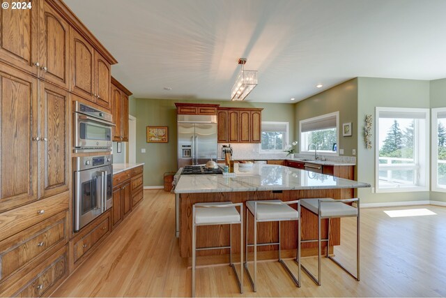 kitchen featuring sink, tasteful backsplash, a kitchen island with sink, appliances with stainless steel finishes, and light hardwood / wood-style floors