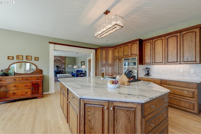 kitchen with pendant lighting, a kitchen island with sink, light hardwood / wood-style flooring, stainless steel appliances, and backsplash