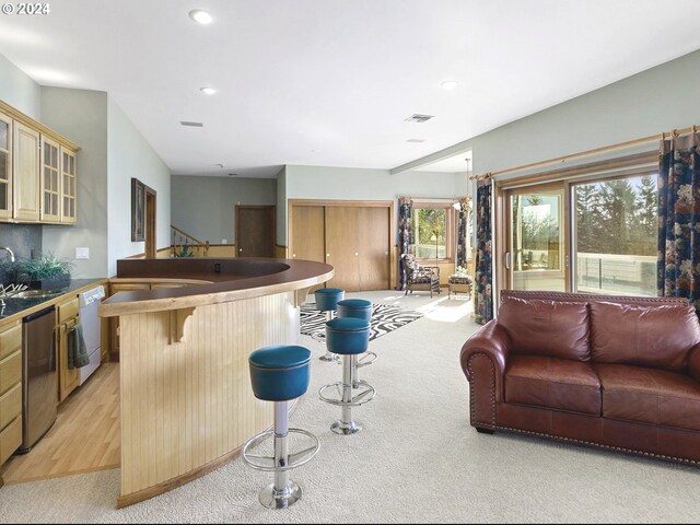 kitchen featuring white dishwasher, sink, dishwasher, a breakfast bar, and light carpet