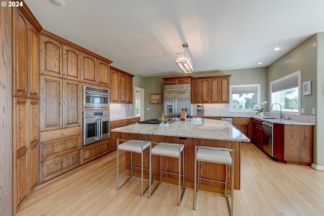 kitchen with appliances with stainless steel finishes, backsplash, light hardwood / wood-style flooring, a center island with sink, and sink