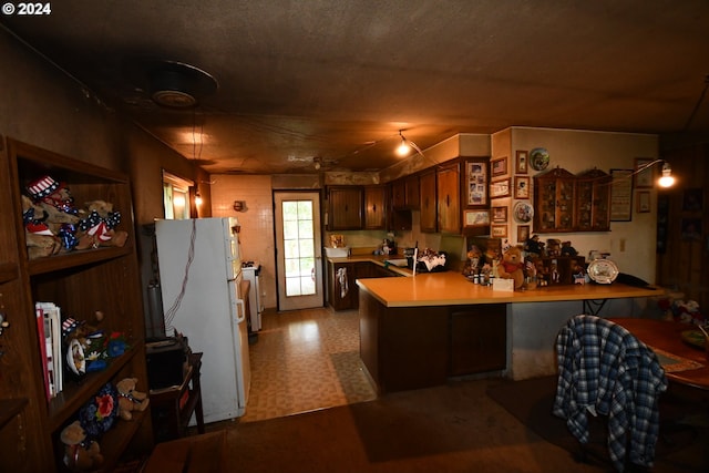 kitchen with tile patterned floors, a peninsula, freestanding refrigerator, light countertops, and a sink