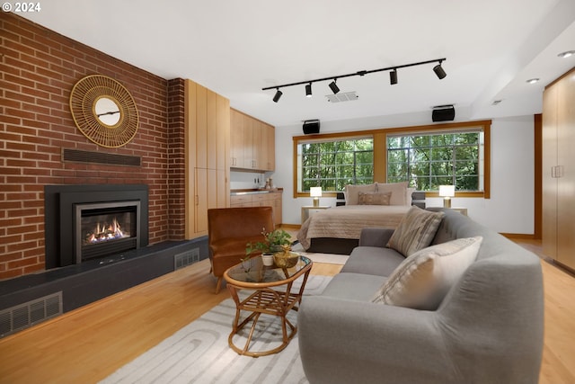 living room featuring a brick fireplace, light wood-type flooring, and rail lighting