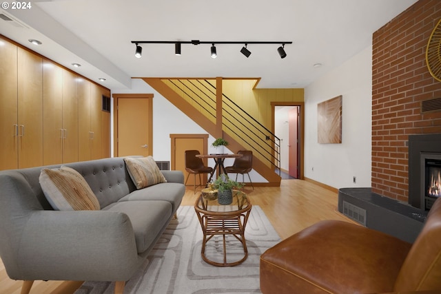 living room featuring track lighting, a brick fireplace, and light hardwood / wood-style flooring