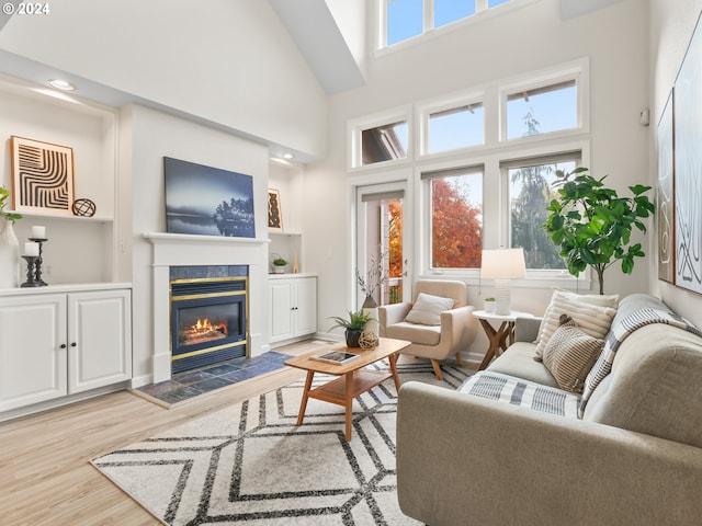 living room featuring light hardwood / wood-style floors, a healthy amount of sunlight, a towering ceiling, and a tile fireplace