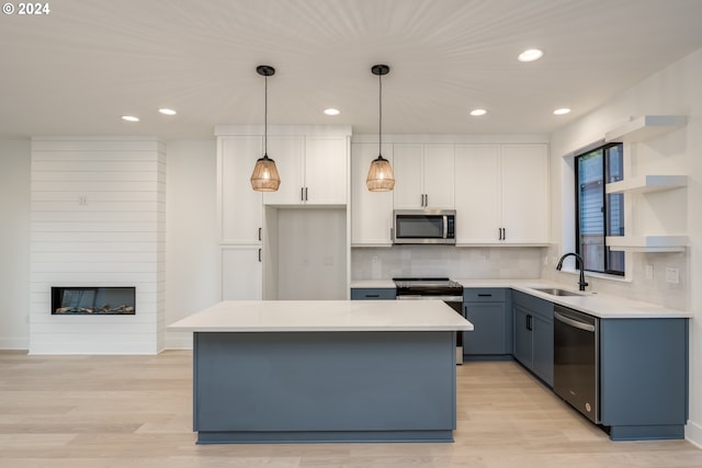 kitchen featuring sink, stainless steel appliances, a kitchen island, decorative light fixtures, and white cabinets