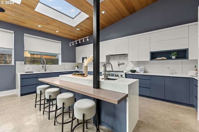 kitchen with backsplash, vaulted ceiling with skylight, a kitchen island with sink, sink, and wooden ceiling