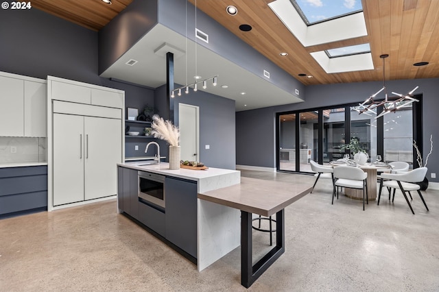 kitchen featuring a skylight, a kitchen island with sink, pendant lighting, wooden ceiling, and white cabinetry