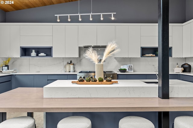 kitchen with decorative backsplash, a kitchen breakfast bar, vaulted ceiling, decorative light fixtures, and white cabinetry