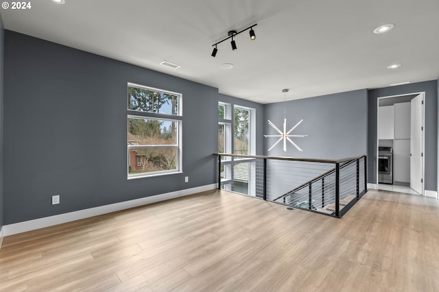 empty room featuring light wood-type flooring, track lighting, and an inviting chandelier