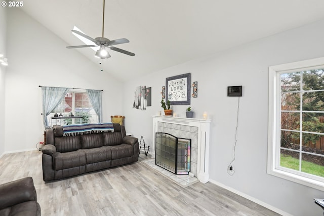 living room with ceiling fan, a tile fireplace, light hardwood / wood-style flooring, and a healthy amount of sunlight