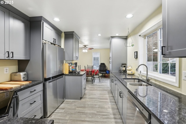 kitchen with decorative light fixtures, stainless steel appliances, dark stone counters, sink, and gray cabinetry