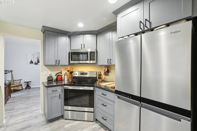 kitchen with gray cabinets, stainless steel appliances, dark stone counters, and light wood-type flooring