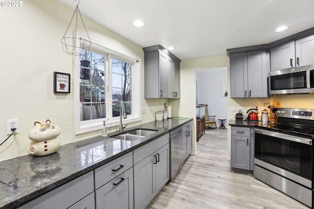 kitchen with pendant lighting, appliances with stainless steel finishes, dark stone countertops, sink, and gray cabinetry