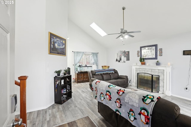 living room with a skylight, ceiling fan, light wood-type flooring, high vaulted ceiling, and a tile fireplace