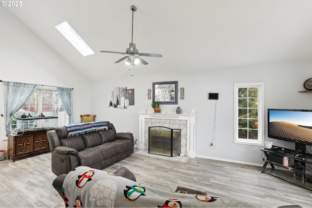 living room featuring a skylight, light hardwood / wood-style floors, a tiled fireplace, and high vaulted ceiling