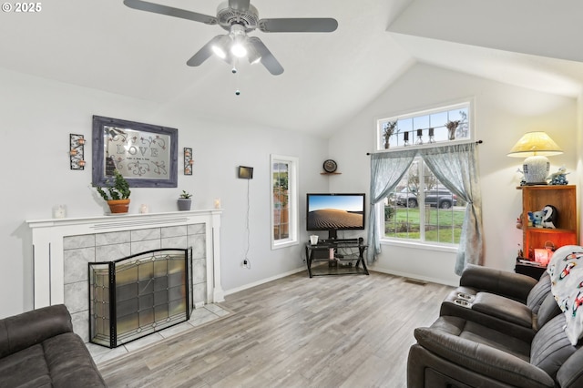 living room with ceiling fan, vaulted ceiling, a tile fireplace, and light hardwood / wood-style floors