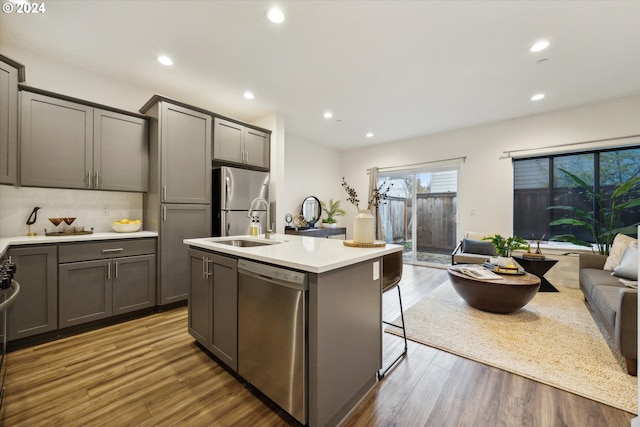 kitchen featuring hardwood / wood-style floors, a center island with sink, gray cabinets, appliances with stainless steel finishes, and a breakfast bar area