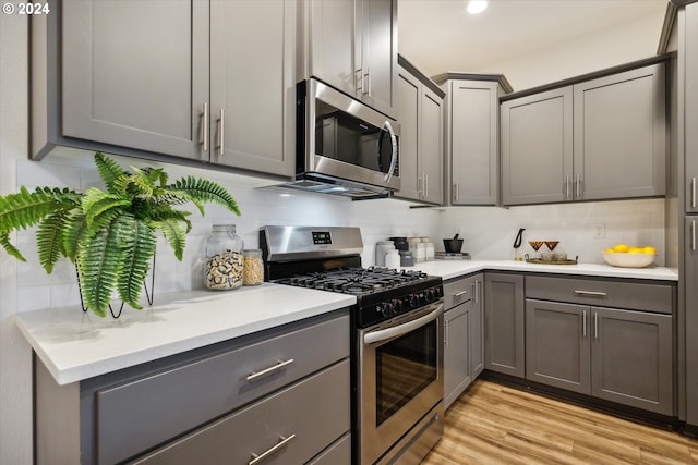 kitchen with light wood-type flooring, stainless steel appliances, gray cabinets, and tasteful backsplash