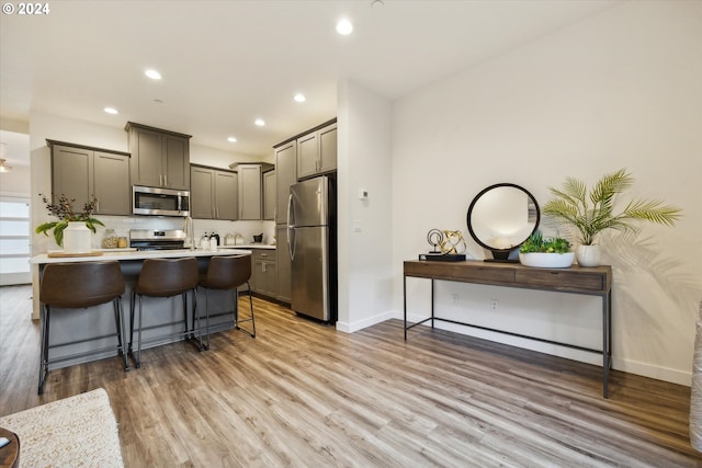 kitchen with gray cabinetry, a kitchen breakfast bar, stainless steel appliances, and light hardwood / wood-style flooring