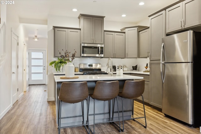 kitchen featuring appliances with stainless steel finishes, a kitchen breakfast bar, gray cabinetry, a kitchen island with sink, and light hardwood / wood-style floors