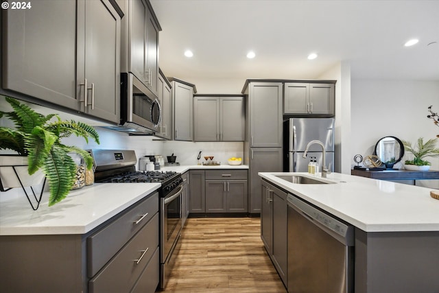 kitchen with appliances with stainless steel finishes, light wood-type flooring, gray cabinetry, and sink