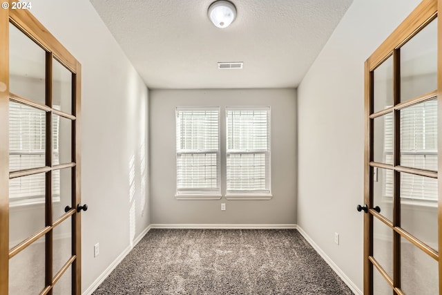 carpeted spare room with french doors and a textured ceiling