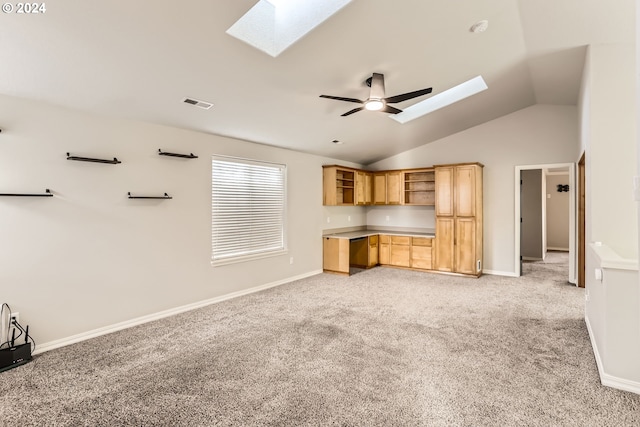 unfurnished living room with light carpet, built in desk, lofted ceiling with skylight, and ceiling fan