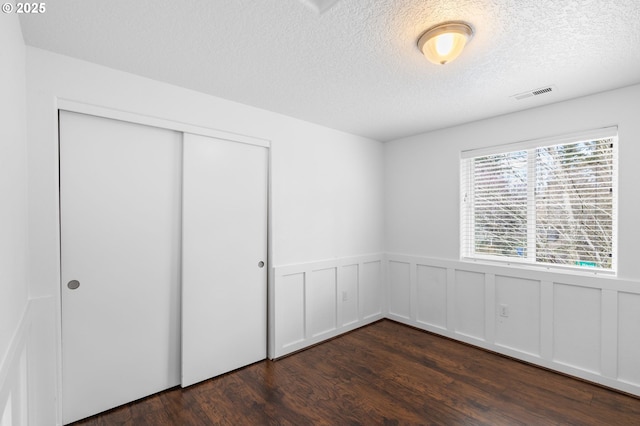 unfurnished bedroom featuring a textured ceiling, visible vents, a closet, wainscoting, and dark wood-style floors