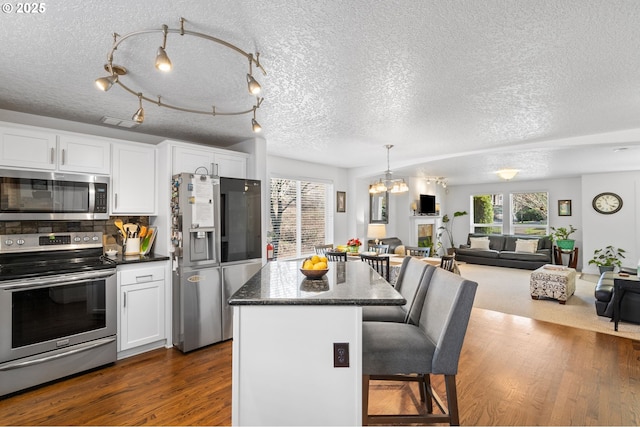 kitchen with appliances with stainless steel finishes, open floor plan, dark wood-style flooring, a kitchen bar, and white cabinetry