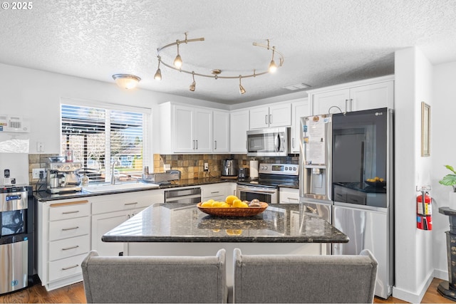 kitchen with dark wood-style flooring, a kitchen island, white cabinets, appliances with stainless steel finishes, and tasteful backsplash