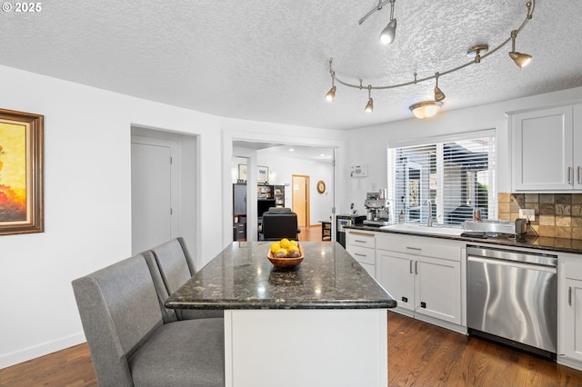 kitchen featuring dark wood-type flooring, dark stone counters, a sink, a center island, and dishwasher