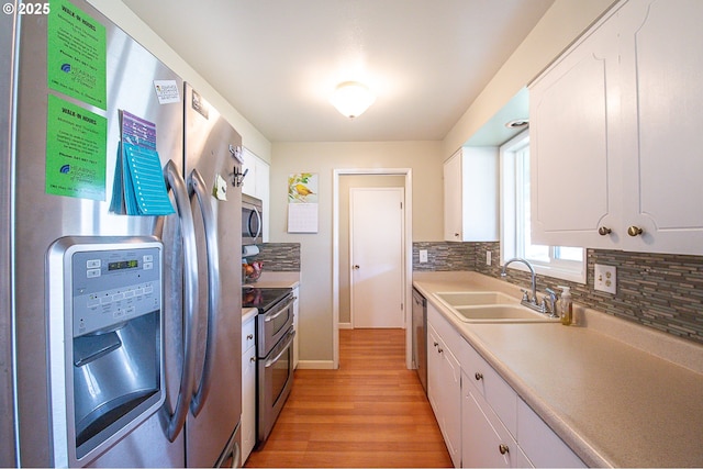 kitchen with appliances with stainless steel finishes, backsplash, sink, light hardwood / wood-style flooring, and white cabinets