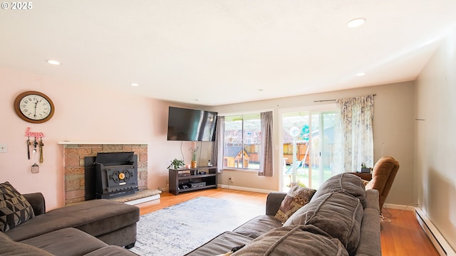 living room featuring light hardwood / wood-style floors, a wood stove, and baseboard heating