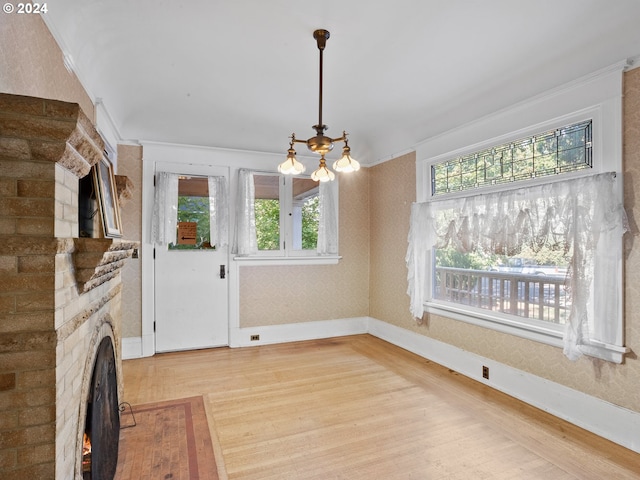 unfurnished dining area with a brick fireplace, a notable chandelier, light wood-type flooring, and a healthy amount of sunlight