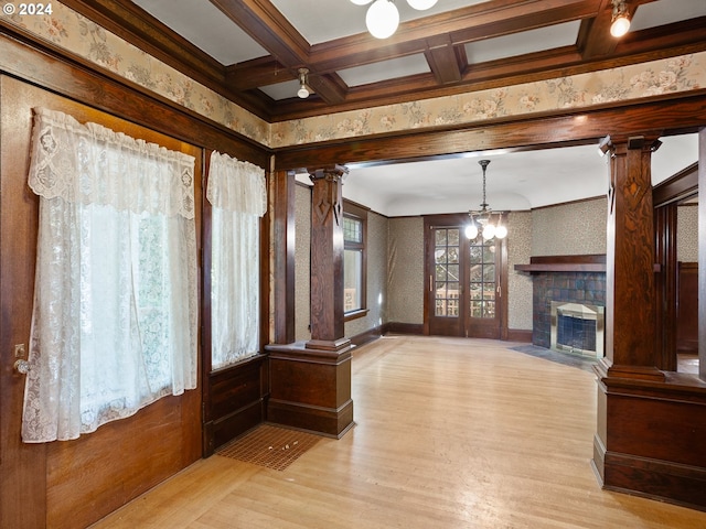 unfurnished living room featuring light wood-type flooring, ornate columns, coffered ceiling, beam ceiling, and a fireplace