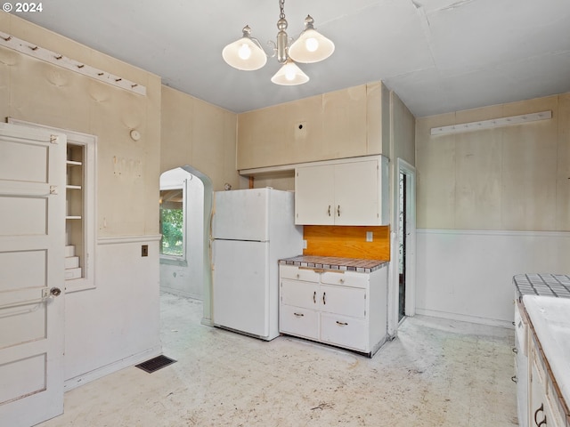 kitchen featuring pendant lighting, white refrigerator, white cabinetry, tile countertops, and an inviting chandelier